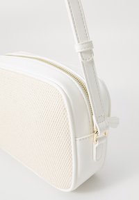 Biała torebka crossbody z teksturowanym panelem z tkaniny, gładką ekoskórą, złotym zamkiem błyskawicznym oraz regulowanym paskiem z klipsem.
