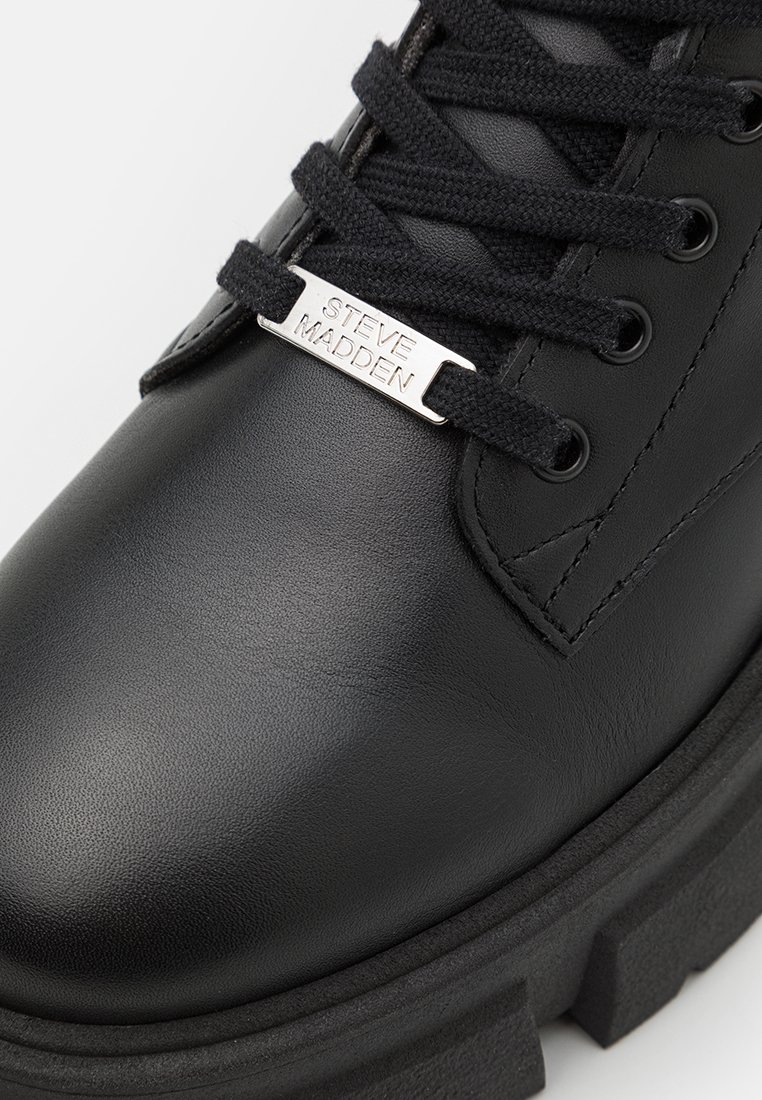 Schwarze Leder-Stiefelette mit runder Zehe, dicker schwarzer Sohle und schwarzen Schnürsenkeln. Mit einem silbernen, gebrandeten Metallplättchen an der Zunge.