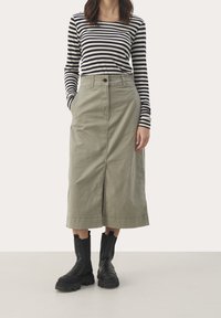 Haut à manches longues rayé bleu marine et blanc, associé à une jupe mi-genou vert olive avec poches latérales et fente avant. Bottes noires épaisses.