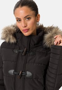 Svart puffjacka med huva kantad med päls, med ett quiltat mönster, läderdetaljer, knappstängningar och ribbade ärmslut.