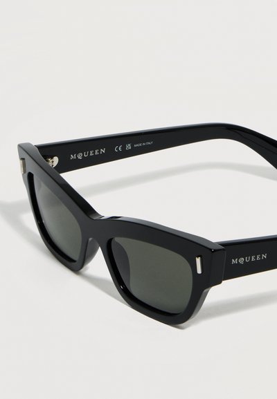 Μαύρα ορθογώνια γυαλιά ηλίου με σκούρους φακούς, παχιά πλαίσια και το λογότυπο "McQueen" στις πλευρές, κατασκευασμένα στην Ιταλία.