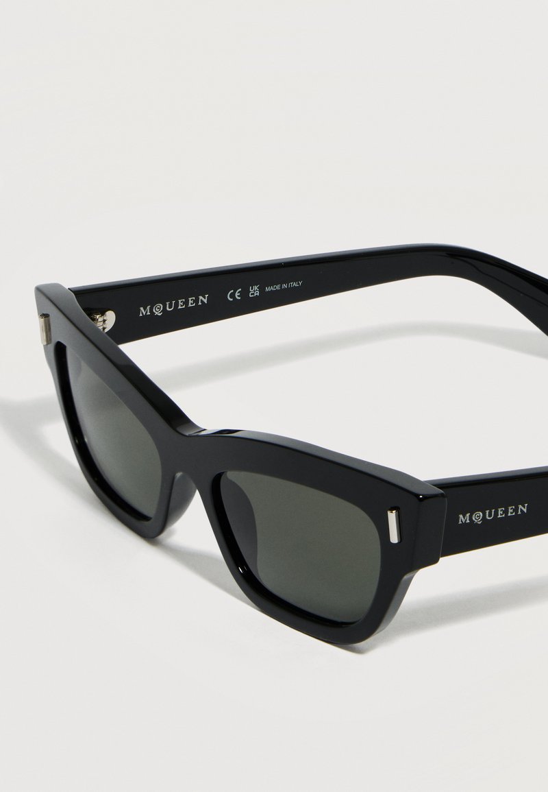 Schwarze rechteckige Sonnenbrille mit dunklen Gläsern, dicken Fassungen und "McQueen"-Markierung an den Bügeln, hergestellt in Italien.