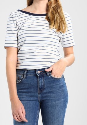 Gestreiftes kurzärmeliges T-Shirt in Creme und Navy mit Rundhalsausschnitt und weichem Baumwollstoff, kombiniert mit eng anliegenden blauen Jeans.