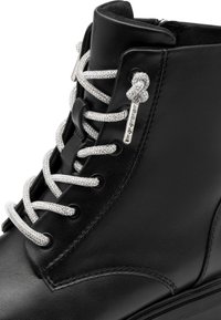 Bottines en cuir noir avec des lacets métalliques argentés, une fermeture éclair et des accents de lacets décoratifs. Texture lisse avec des détails de couture.