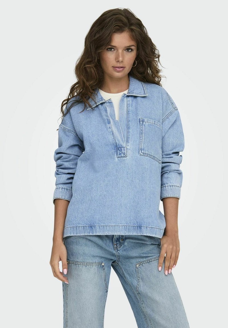 Suéter de denim azul claro con cuello, bolsillo frontal y manga larga. Combinado con jeans azul claro a juego, que presentan un ajuste relajado.