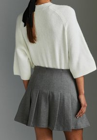 Maglione bianco, peloso, con maniche corte e larghe abbinato a una gonna grigia plissettata. L'outfit presenta una consistenza morbida e un design lineare.