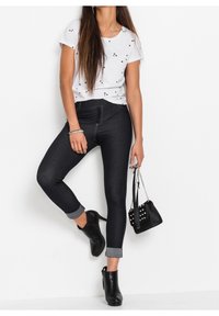 Biała koszulka z nadrukiem czarnej gwiazdy, zestawiona z ciemnymi dżinsowymi legginsami z podwiniętymi mankietami i zamkiem błyskawicznym z przodu. Czarne botki i mała czarna torebka.