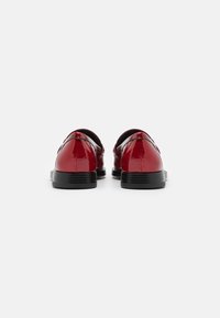 Sapatos de couro vermelho brilhante, com bico arredondado, salto preto baixo e textura lisa, apresentando um design simplista sem adornos.