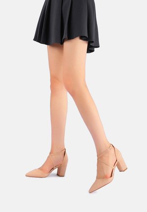 Décolleté beige con punta affusolata, finitura texturizzata, tacco a blocco e fasce incrociate alla caviglia. Design curvo che esalta le gambe.