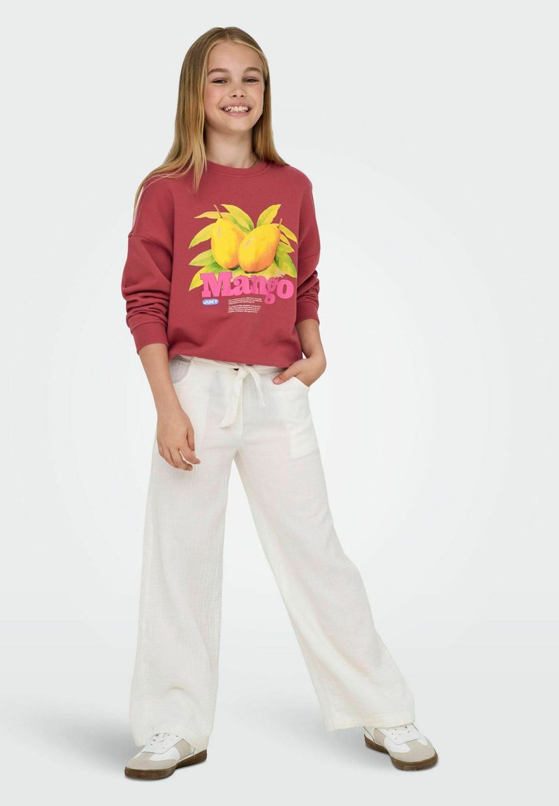 Röd sweatshirt med ett mango-mönster och vit text, matchad med vida vita byxor. Utseendet kompletteras av vita sneakers.