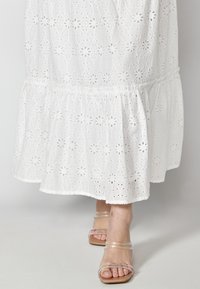 Vit broderad bomulls klänning med volangkjol, med blommönster och genomskinliga detaljer, som matchas med klara remsandaler.