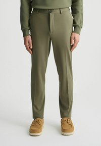 Pantalones verde oliva hechos de una tela suave, con un bolsillo frontal y un cierre de botón, combinados con zapatos de ante color marrón claro.