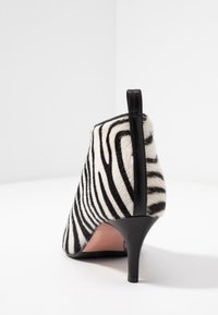 Zwart-witte gestreepte hak met een textuur van bont als bovenmateriaal, een spitse neus en een slanke zwarte hak. De achterkant toont het ontwerp.