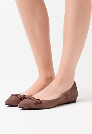 Ballerines en daim marron avec un détail de nœud à l'avant, forme arrondie et semelle basse et flexible. Texture lisse et design minimaliste.