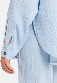 Lichtblauwe, gestructureerde blouse met lange mouwen, voorzien van uitsnijdingen en knoopmanchetten, die een ontspannen, vloeiende uitstraling heeft.