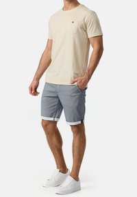 Light beige short-sleeve shirt with a chest pocket, paired with blue patterned shorts with rolled hems and white sneakers.