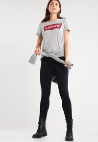 Grå bomulds T-shirt med et rødt Levi's-logo, parret med sorte slim-fit jeans og sorte snørebåndsstøvler. T-shirten er knyttet i taljen.