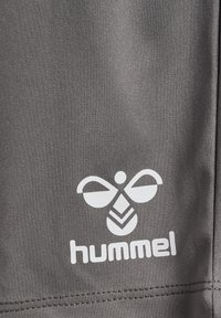 Grått tyg med en strukturerad mönstring, med en vit Hummel-logotyp som liknar en stiliserad bi i nedre högra hörnet.