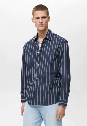 Camicetta button-up blu navy con strisce verticali bianche, maniche lunghe e taschino sul petto. Realizzata in un tessuto leggero con una texture morbida.