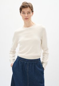 Kremno barvana pletena pulover s okroglo izreza, v kombinaciji z temno denim krilom z elastiko in stranskimi žepi.