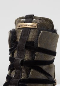 Botte en cuir vert olive à lacets avec des accents en suède noir, finition texturée et plaque logo en bronze en haut. Dispose d'une doublure en fourrure.