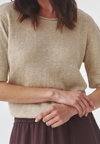 Jersey de punto beige con mangas cortas, escote redondo y corte ancho. La tela tiene una textura suave con un patrón sutil de tejido abierto.