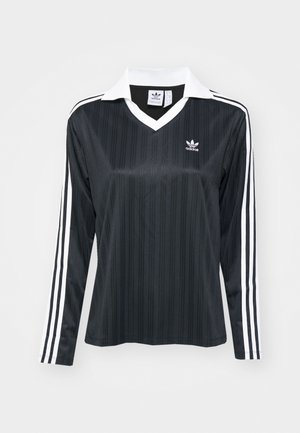 Chemise noire à manches longues avec un col blanc, texture verticale et trois rayures blanches le long de chaque manche. Présente un logo brodé.