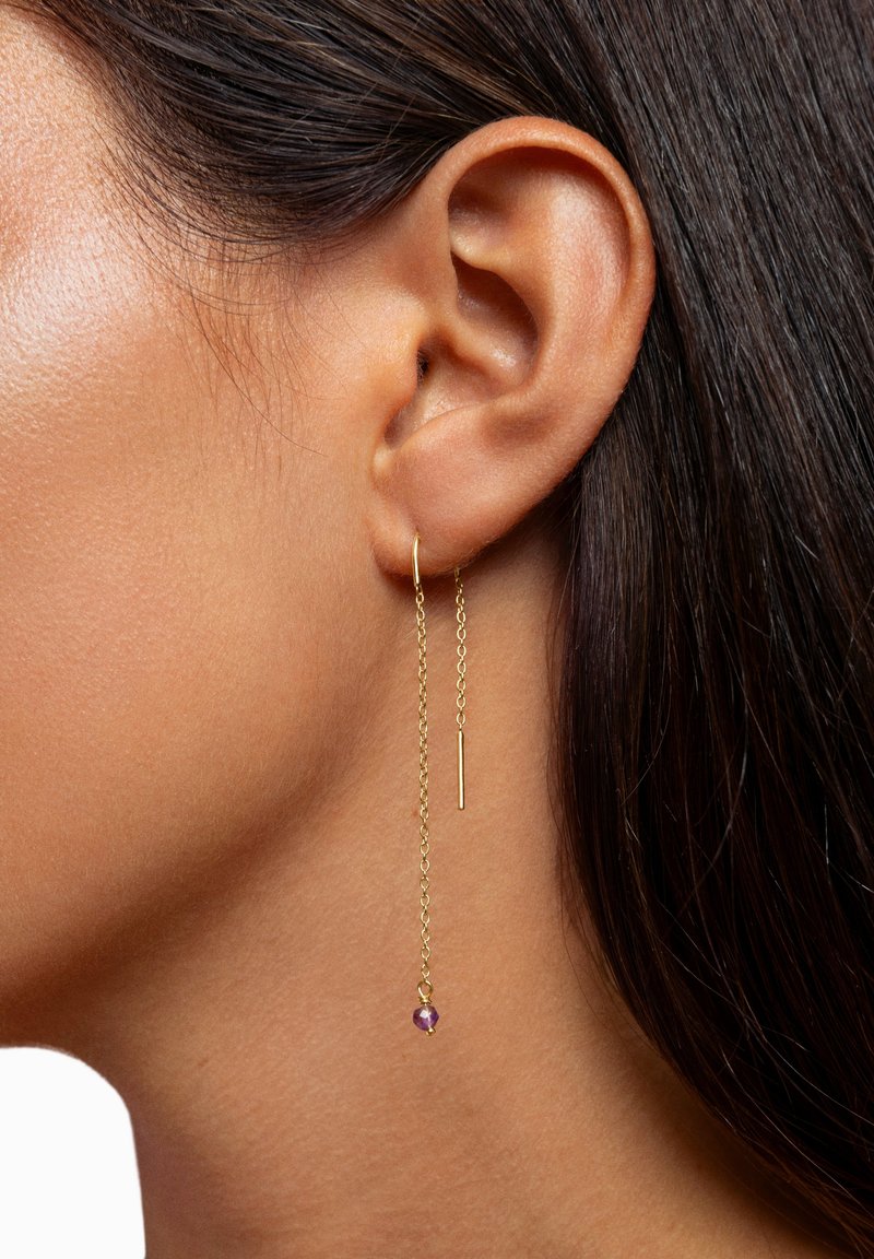 Goldene Kettenohrringe mit einem vertikalen Stab und einem kleinen violetten Edelstein, der zart von der Kette hängt. Sie haben ein minimalistisches Design.
