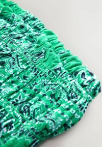 Gros plan sur un tissu vert avec des motifs floraux et cachemire, présentant une couture élastique froncée le long du bord.