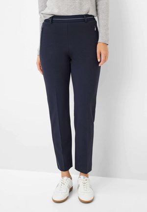 Donkerblauwe aansluitende broek met een zachte textuur, met twee zijzakken met rits en een riemlus tailleband, gecombineerd met witte sneakers.