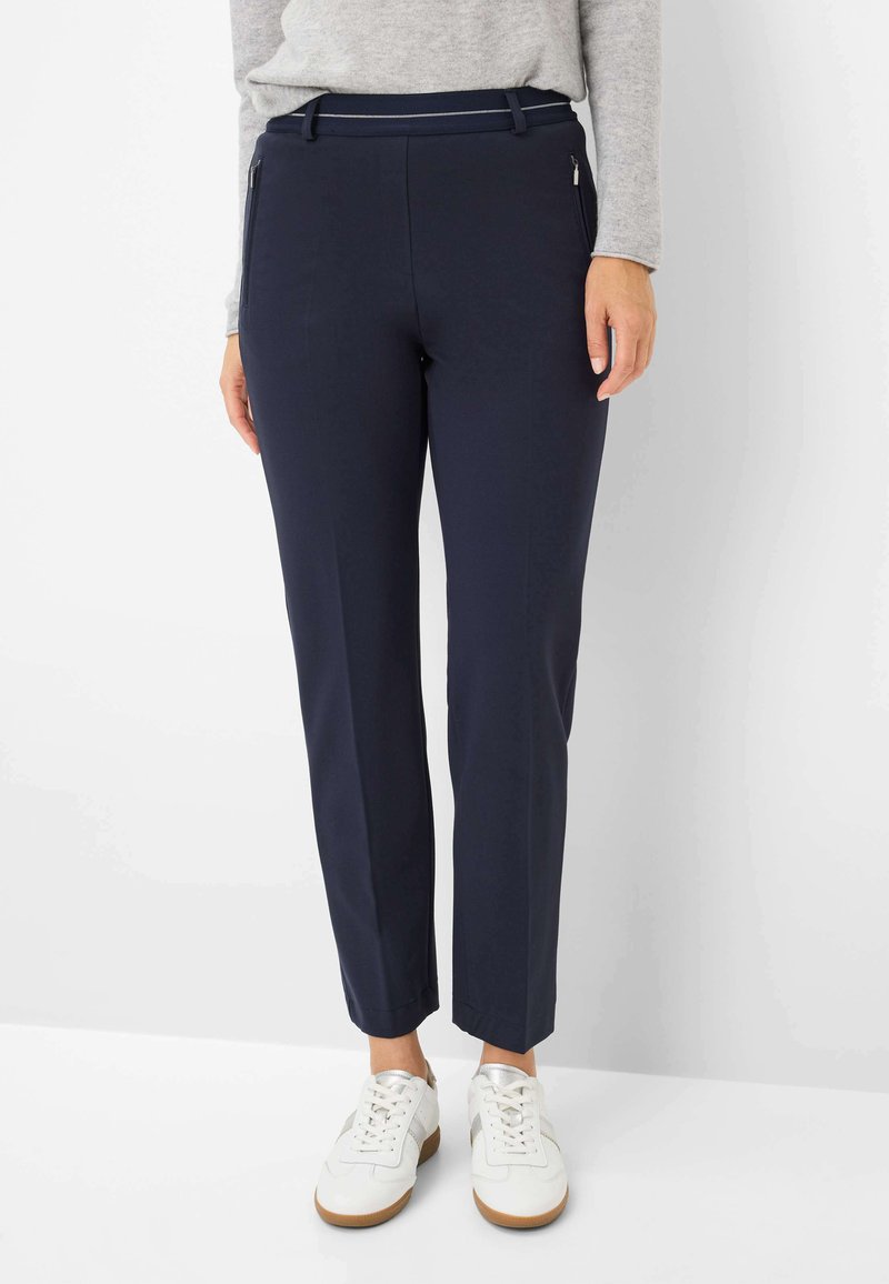 Donkerblauwe aansluitende broek met een zachte textuur, met twee zijzakken met rits en een riemlus tailleband, gecombineerd met witte sneakers.