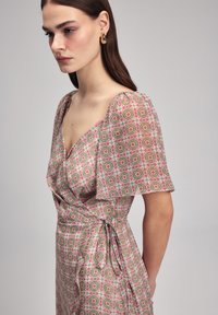 Kleid mit Blumendesign, kurzen, flatternden Ärmeln, V-Ausschnitt und Taillengürtel; besteht aus einem leichten Stoff in Grün-, Pink- und Weißtönen.