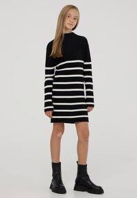 Abito a maglia a righe bianche e nere con collo alto e maniche lunghe, abbinato a stivali alla caviglia neri. Tessuto liscio.