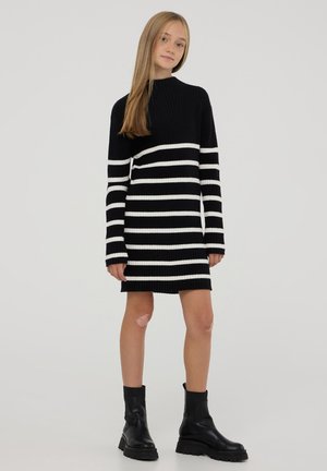 Abito a maglia a righe bianche e nere con collo alto e maniche lunghe, abbinato a stivali alla caviglia neri. Tessuto liscio.
