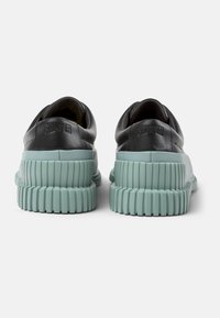 Zapatillas de cuero negro con una superficie texturizada, que cuentan con una gruesa suela de goma verde menta y un logo de la marca en relieve en el talón.