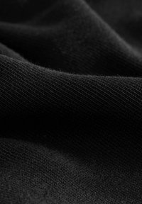 Svart stickad tyg med en slät yta och subtilt ribbat mönster. Materialet verkar mjukt och flexibelt, vilket skapar mjuka veck och draperingar.