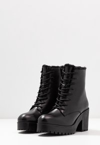 Zwarte leren enkelboots met een stevige hoge hak, veter sluiting aan de voorkant en een zachte voering aan de bovenkant. Getextureerde rubberen zool met grip.