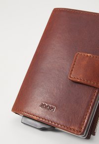 Brun lærwallet med en teksturert overflate, som har en frontklaff, preget logo og metallkortholder som stikker ut fra siden.