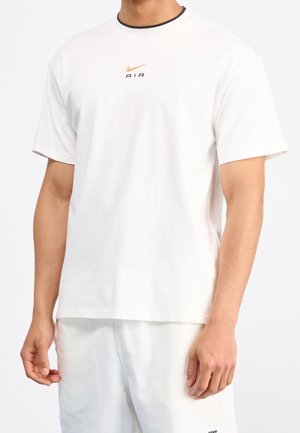 Biała bawełniana koszulka z krótkim rękawem, okrągłym dekoltem, ozdobiona małym czarno-złotym logo Nike. Gładka faktura, luźny fason.