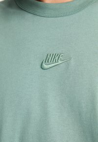 T-shirt verde de algodão com um logótipo da Nike cosido na mesma tonalidade. Design de gola redonda com um acabamento suave e texturizado.