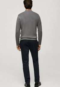 Grå tröja med rund hals, används tillsammans med mörka byxor. Materialen ser släta ut med en figursydd design, sedd bakifrån.