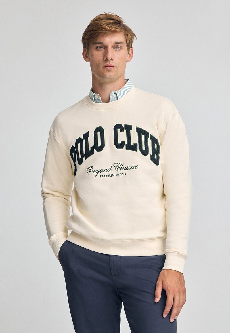 Felpa color crema con la scritta "POLO CLUB" in lettere verde scuro. Collo rotondo, maniche lunghe, tessuto morbido e polsini a costine.