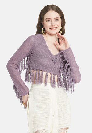 Paarse cropped trui met lange mouwen, voorzien van franjen langs de zoom. Gepenetreerd met witte, gestructureerde broek met hoge taille.