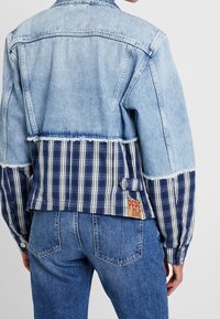 Kurtka dżinsowa z jasnoniebieskim górnym fragmentem i ciemnoniebieskim, w kratę, dolnym fragmentem, z postrzępionymi krawędziami i wyraźną metką Pepe Jeans.