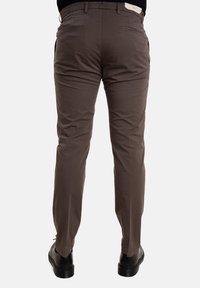 Pantaloni marroni con una texture liscia, dotati di tasche posteriori e una vestibilità su misura. Abbinati a scarpe nere per un look completo.