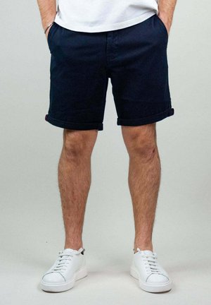 Pantaloni corti in cotone blu navy con risvolti, tasche laterali e vestibilità slim. Abbinati a sneakers bianche stringate per un look casual.