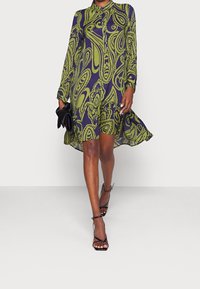 Långärmad klänning med ett mönster i grön och marinblå paisley, krage, knäppning framtill och en tiered nederkant; matchad med svarta sandaletter med remmar.