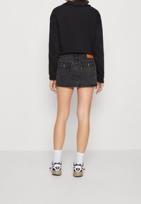 Černá džínová minisukně s vybledlou texturou, pěti kapsami a koženým zadním štítkem. V kombinaci s černým topem s dlouhým rukávem a bílými ponožkami.