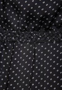 Svart tyg med vita cirkulära prickar, med ett strukturerat, flätat midjeband och mjukt fall.