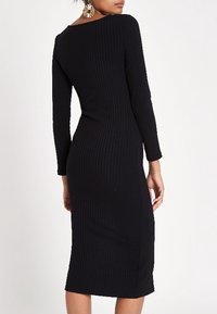 Robe midi noire côtelée avec une silhouette ajustée, manches longues et encolure bateau, présentant une texture lisse et un design minimaliste.